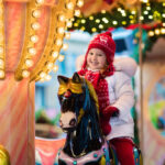 A photograph of a little girl riding on a merry-go-round during the holiday season.