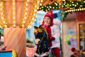 A photograph of a little girl riding on a merry-go-round during the holiday season.